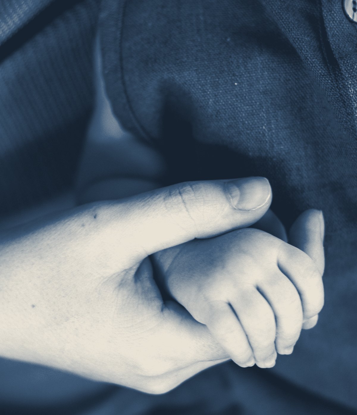 An adult and newborn gently holding hands